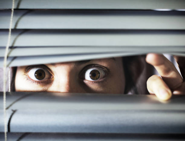 istock Terrified young woman looking through blinds 1166345669