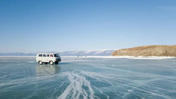 An old excursion off-road bus rides on the ice of the frozen lake Baikal in Siberia. The bright winter journey through Russia. Irkutsk region.