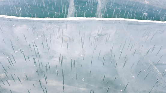 The ice surface of lake Baikal in the spring month. Bubbles in the form of long needles are visible under the ice. The color of the water is blue and greenish. Bright winter in Siberia.