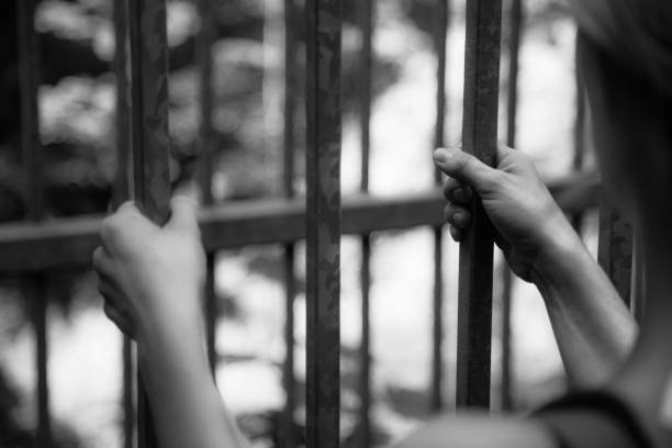 istock Prison cell: Close up of hands in jail 1166347276