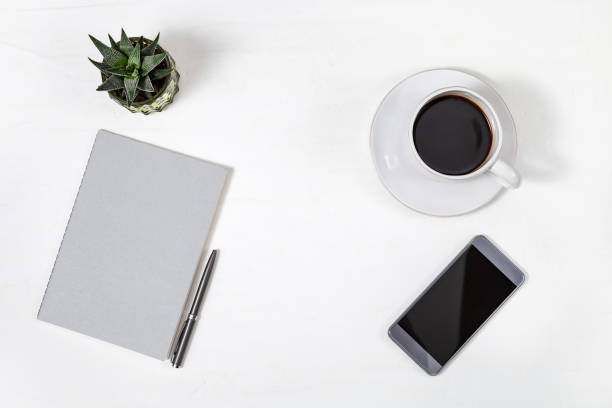 istock White minimal office desk table with smartfone, grey closed copybook, pen and small cactus plant, cup of coffee. Top view with copy space. Flat lay. 1166348428