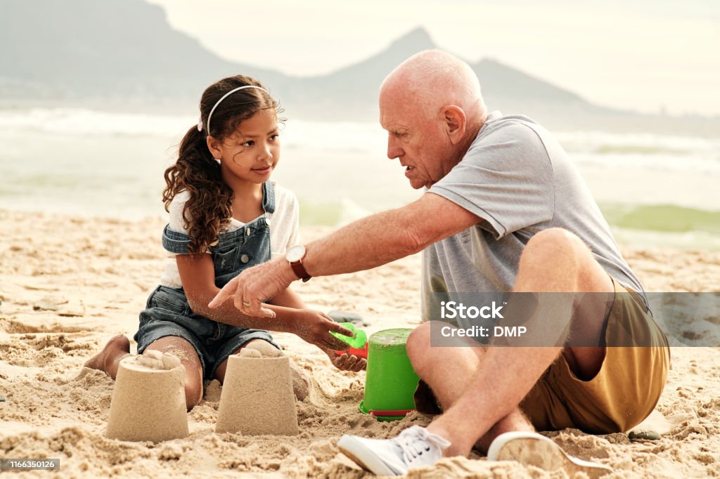 Making sure she has a solid foundation in life Full length shot of an adorable little girl playing with her grandfather in the sand at the beach Beach Stock Photo Making sure she has a solid foundation in life Full length shot of an adorable little girl playing with her grandfather in the sand at the beach Beach Stock Photo