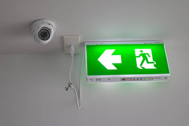 istock Modern CCTV camera on a wall with LED exit sign,  Close-up Exit neon or led sign in corridor point way out of resident apartment building 1166353188