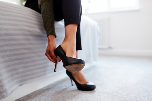 Close Up Of Businesswoman At Home Sitting On Bed Putting On Shoes Before Leaving For Work