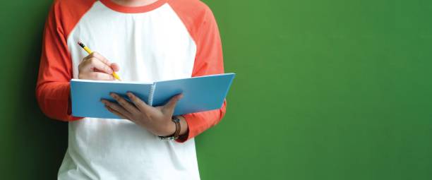 High school, university student in casual writing on paper notebook, Teenager student writing notebook standing in fornt of green wall with copy space at school campus, College education secundaria, estudiante universitario en escritura casual en cuaderno de papel, adolescente estudiante escribiendo cuaderno de pie en la parte superior de la pared verde con espacio de copia en el campus de la escuela, educación universitaria