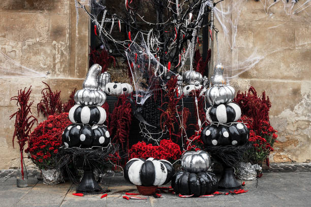 Painted black and white pumpkins for Halloween. Festive composition with red flowers and gourds near house