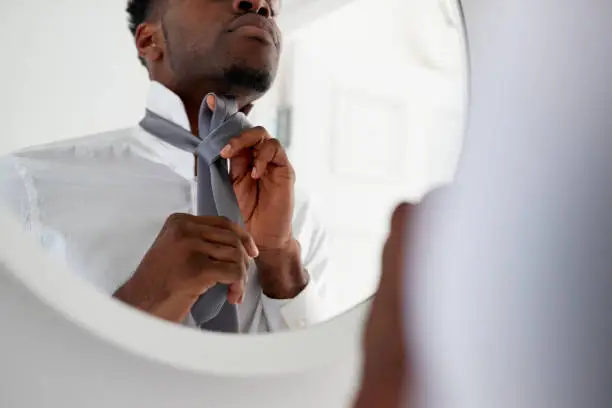 Businessman At Home Tying Necktie In Mirror Before Leaving For Work