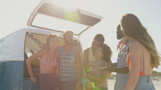 Young adult friends standing by a camper van at a beach 4k