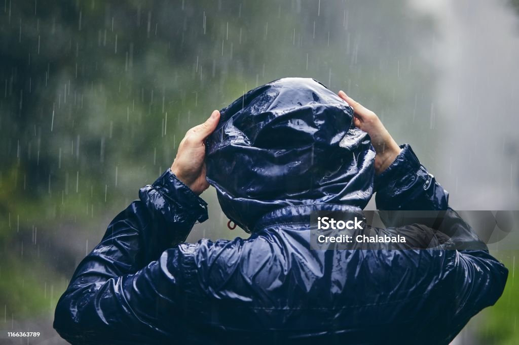 Traveler in heavy rain Trip in bad weather. Rear view of young man in drenched jacket in heavy rain. Raincoat Stock Photo