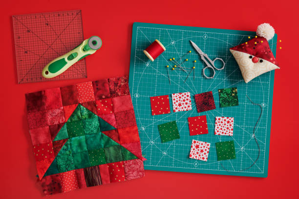 christmas tree patchwork block, craft mat, bright square pieces of fabric, pincushion like santa and quilting accessories on red background - christmas quilt craft patchwork imagens e fotografias de stock