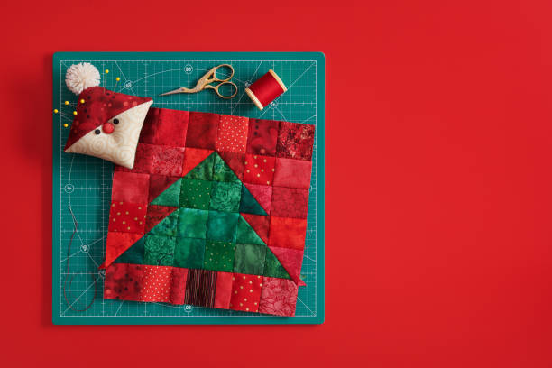christmas tree patchwork block, pincushion like santa, scissors, spool of thread on craft mat, red background - quilt textile patchwork thread imagens e fotografias de stock