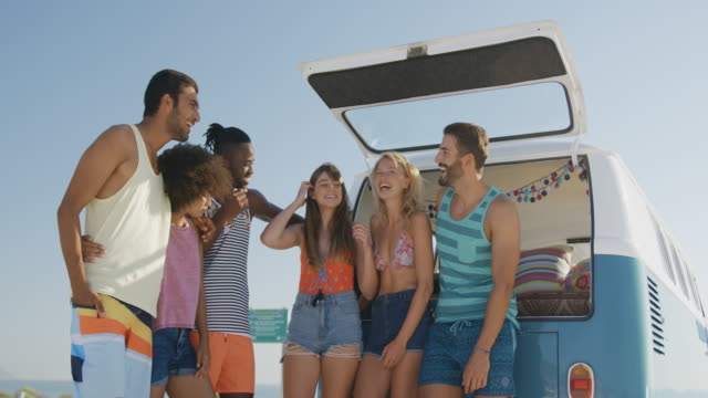 Young adult friends standing by a camper van at a beach 4k