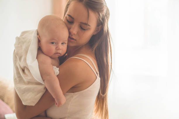 Home portrait of a newborn baby with mother on the bed. Mom holding and kissing her child Home portrait of a newborn baby with mother on the bed. Mom holding and kissing her child. Concept breast feeding cute boy show love symbol hand stock pictures, royalty-free photos & images