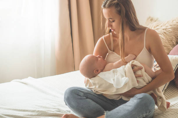 Home portrait of a newborn baby with mother on the bed. Mom holding and kissing her child Home portrait of a newborn baby with mother on the bed. Mom holding and kissing her child. Concept breast feeding cute boy show love symbol hand stock pictures, royalty-free photos & images