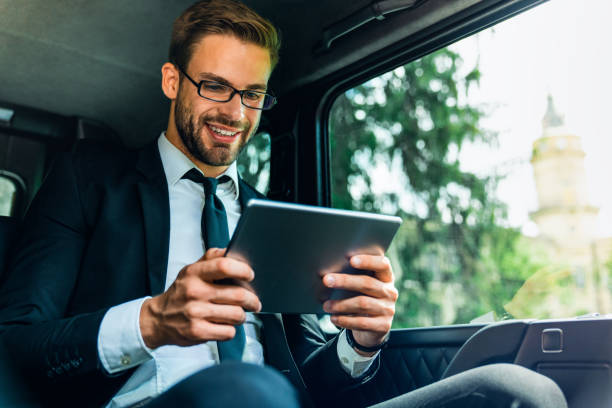 istock Smiling young man in full suit working using digital tablet while sitting in the car 1166366831