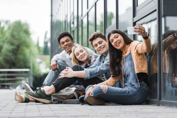 happy friends smiling, sitting and taking selfie with smartphone happy friends smiling, sitting and taking selfie with smartphone teenagers only stock pictures, royalty-free photos & images