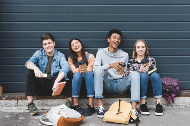 happy teenagers sitting, smiling, holding paper cups and looking at camera happy teenagers sitting, smiling, holding paper cups and looking at camera teenagers only stock pictures, royalty-free photos & images