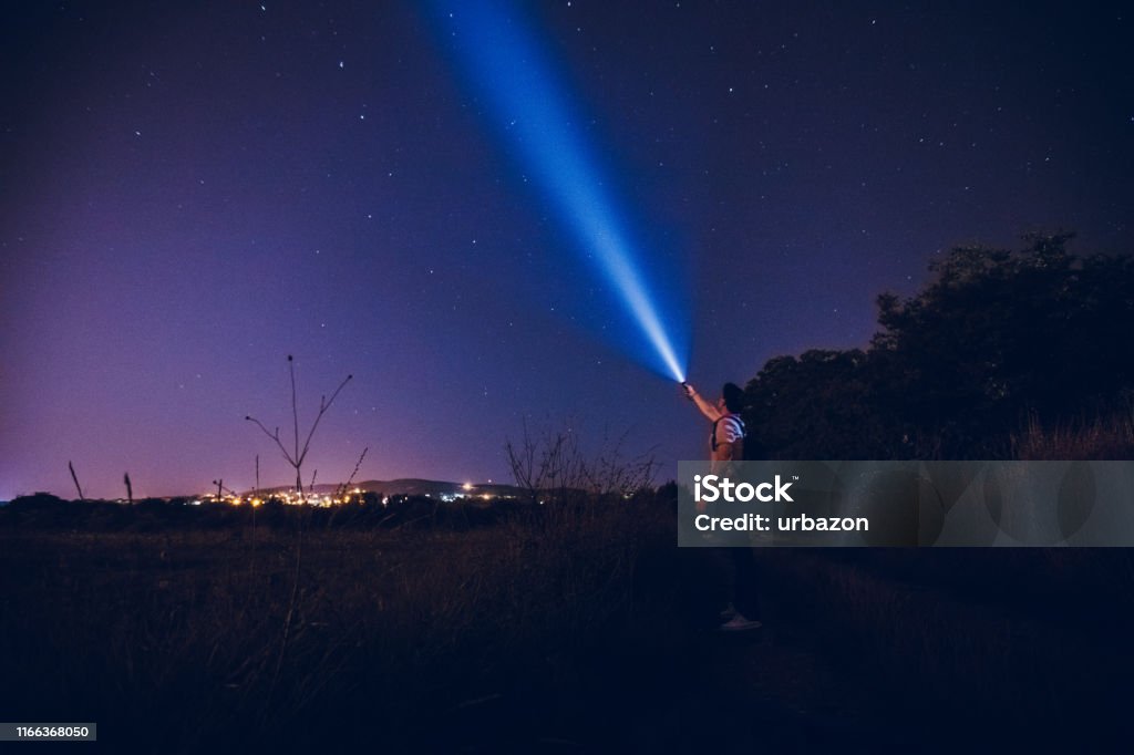 Man lighting up the stars Young caucasian man in the night, with a lantern in the hand doing a beam of light on a sky of stars. Stars exploring. Lighting Equipment Stock Photo