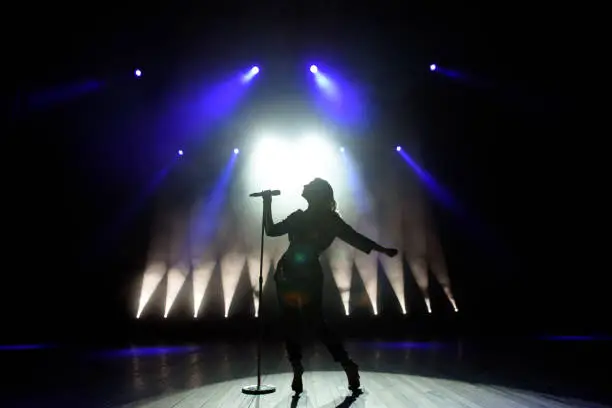 Photo of Silhouette of singer on stage. Dark background, smoke, spotlights.