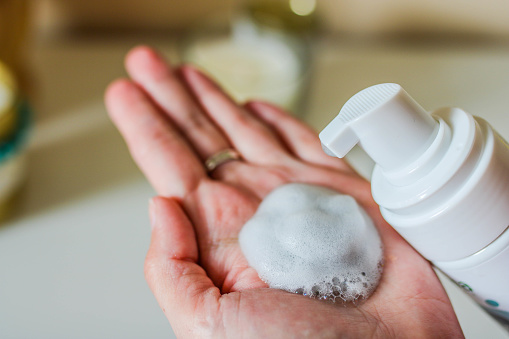 Limpiador facial en la mano femenina y el recipiente de la bomba de espuma cosmética. Fondo borroso blanco. photo
