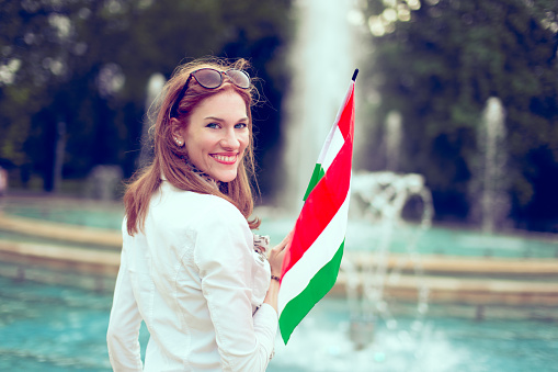 Happy young woman holding Hungarian flag at fountain, looking back, Margaret Island, Budapest, Hungary