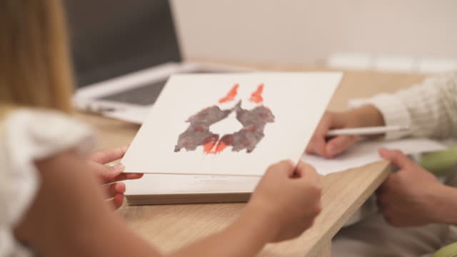 Close-up of a psychologist showing Rorschach inkblot image to her teenage patient and writing down the results. Selective focus shot