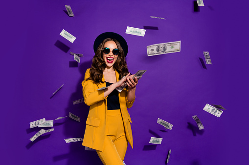 Portrait of her she nice attractive cheerful cheery positive trendy luxury wavy-haired lady throwing 100 hundred million expenses isolated over bright vivid shine violet lilac background
