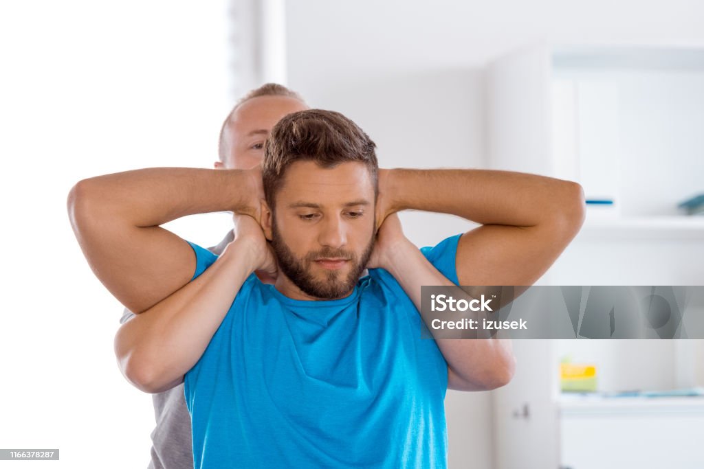 Physiotherapist massaging young man Young man getting massage from physiotherapist at medical center. Physiotherapist doing massage to young man in medical office. Chiropractic Adjustment Stock Photo