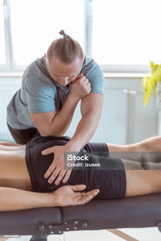 Physiotherapist massaging hips of young man Male physiotherapist massaging hips of a man using his elbow at rehab center. Physiotherapist giving massage to young man at medical center. Buttocks Stock Photo
