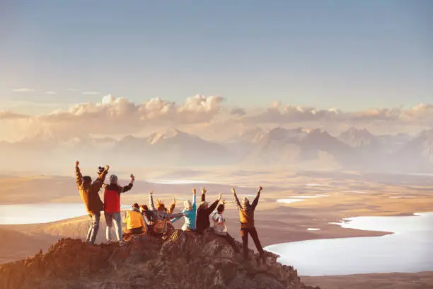 Large group of happy friends is having fun on mountain top and looks at mountain's valley. Adventure or travel concept
