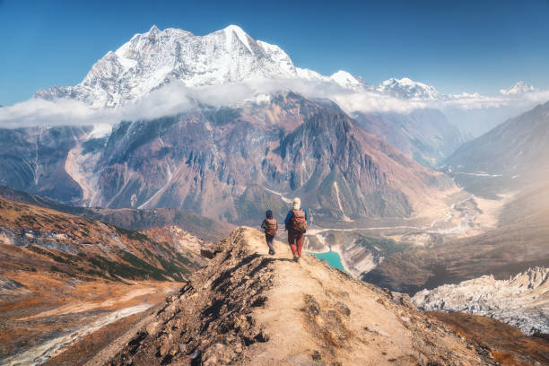 晴れた日に登山道を歩く人々。バックパックを持つ男女の風景、雪のピークを持つ高い山、雲の岩、青い空。活発な人々。ネパールの旅行。トレッキング - footpath single lane road sunrise landscape ストックフォトと画像