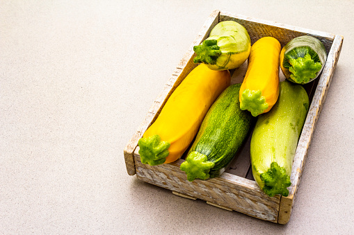 Assorted colorful zucchini in wooden box. Fresh vegetables for cooking. Harvest on stone background, copy space