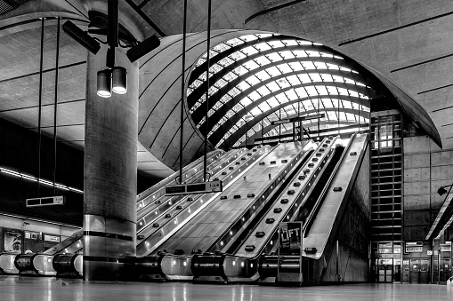 London, UK - July 31 2018: Illustrative editorial in black and white of the the main escalators in the interior of Canary Wharf tube station in London, England