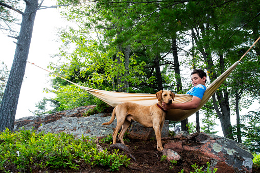 A teen boy and his dog relax in a beautiful woodland setting