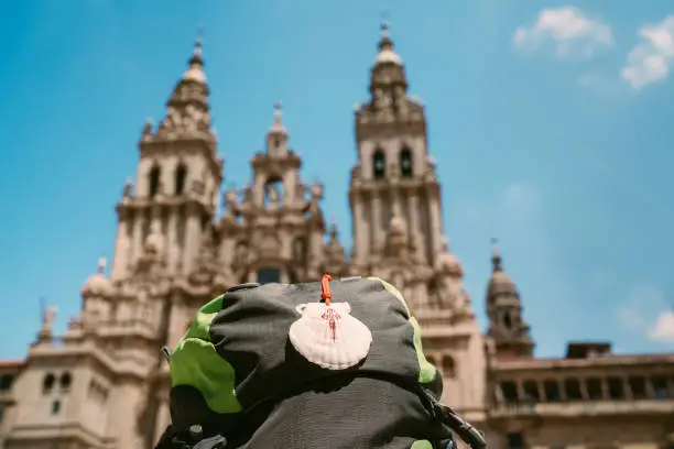 Pilgrim's backpack with famous pilgrims' mascot and sign seashell with Cross of Saint James at  on the Obradeiro square (plaza) - the main square in Santiago de Compostela with Catedral de Santiago.