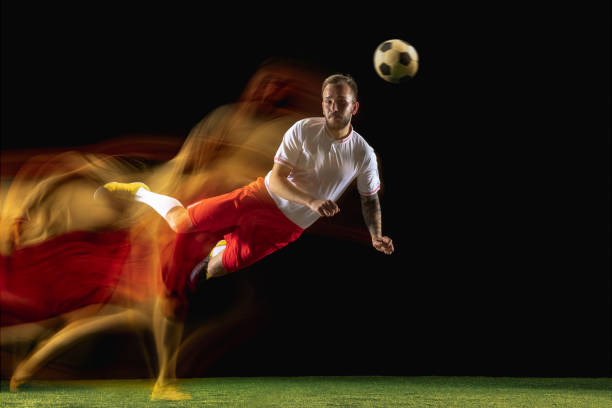 istock Male soccer player kicking ball on dark background in mixed light 1166392676