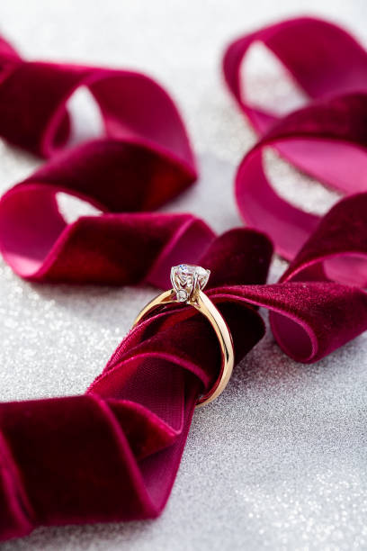 istock Wedding diamond ring on white glossy background with burgundy ribbon 1166392744
