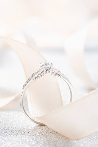 Silver wedding diamond ring on white sparkle background with beige ribbon