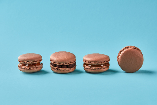 Close-up studio shot of four delicious chocolate macarons on blue background. French pastry cookies with chocolate cream. Copy space.