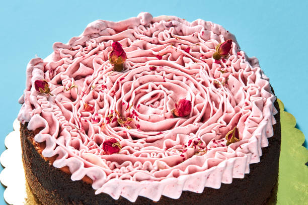 Delicious pink cream cake decorated with a small dried rosebuds, standing on a gold stand against a blue studio background