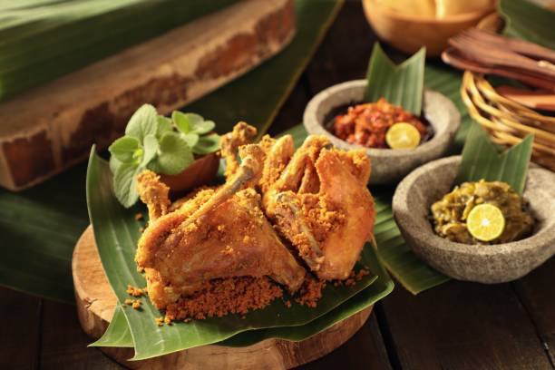 Ayam Goreng Padang, the Fried Chicken Dish with Spice Crumbs from Minangkabau, West Sumatra Ayam Goreng Padang, the traditional fried chicken dish with spice crumbs from Minangkabau cuisine in West Sumatra. Plated on a wooden cutting block lined with banana leaf and garnished with cumin leaves. Served with two kinds of chili sauce on stoneware mortars. drumstick stock pictures, royalty-free photos & images