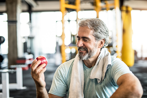 Mature man eating an apple in a gym.