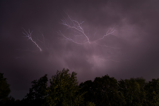 Rainy sky on a summer night with a flash of lightning on the left side of the sky, with the roofs of rural buildings.