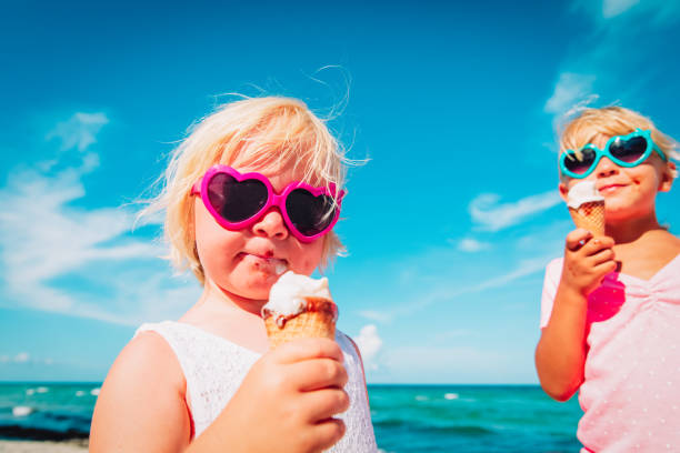 happy cute little girls eating ice cream on beach happy cute little girls eating ice cream on beach vacation licking ice cream cone stock pictures, royalty-free photos & images