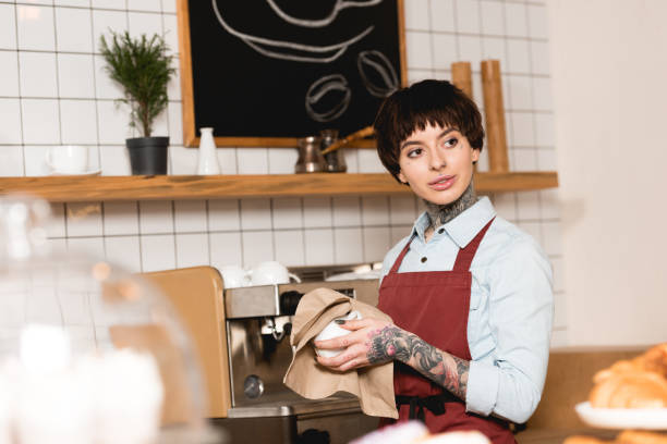 istock selective focus of pretty barista wiping cup while standing near espresso machine 1166407013