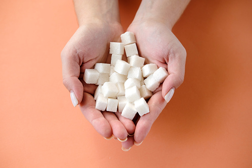 Woman holding in hands white sugar cubes  on orange background. Diabetes, sugar disease, unhealthy food, diet concept. Copy space