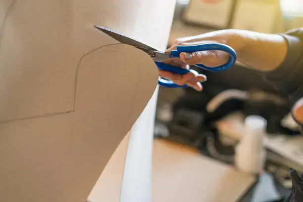 Photo of Close up on hands holding paper cardboard cutting using scissors at home office