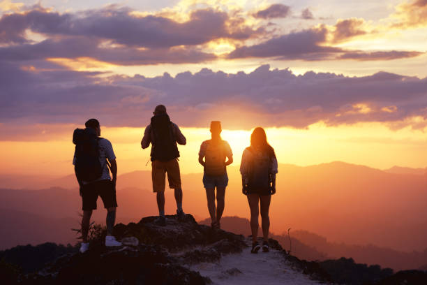 Group tourists friends peoples mountain top look sunset Group of four tourists or friends stands on mountain top and looks at sunset. Peoples travel concept group of people people recreational pursuit climbing stock pictures, royalty-free photos & images