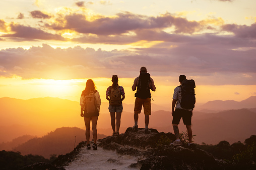 Group of four people's silhouettes stands on mountain top and looks at sunset
