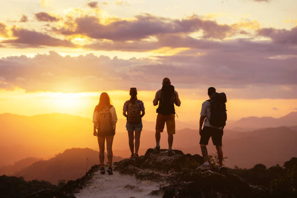 Four people's silhouettes on mountain top looks at sunset stock photo